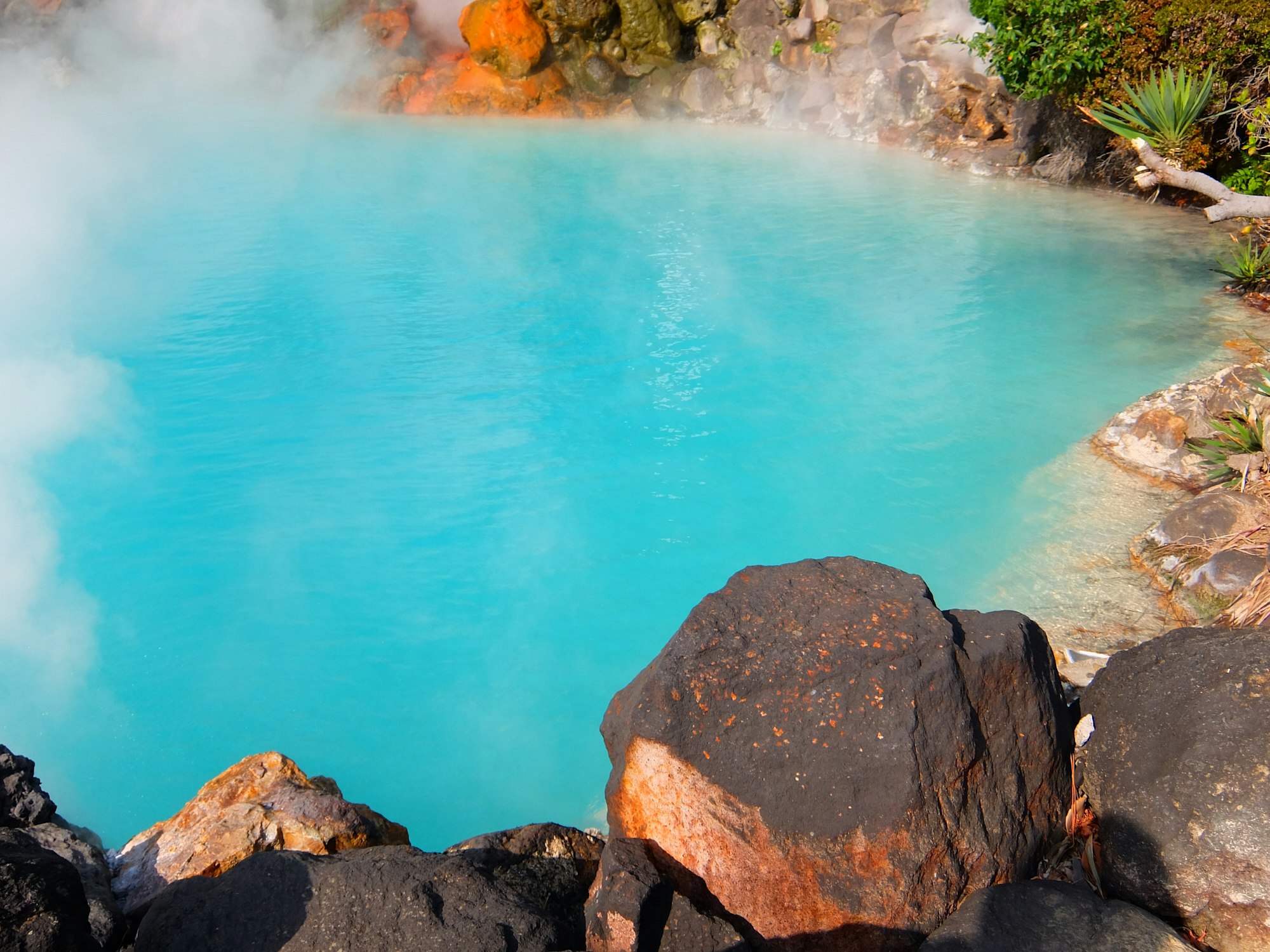 Lava rocks beside turquoise color hot spring